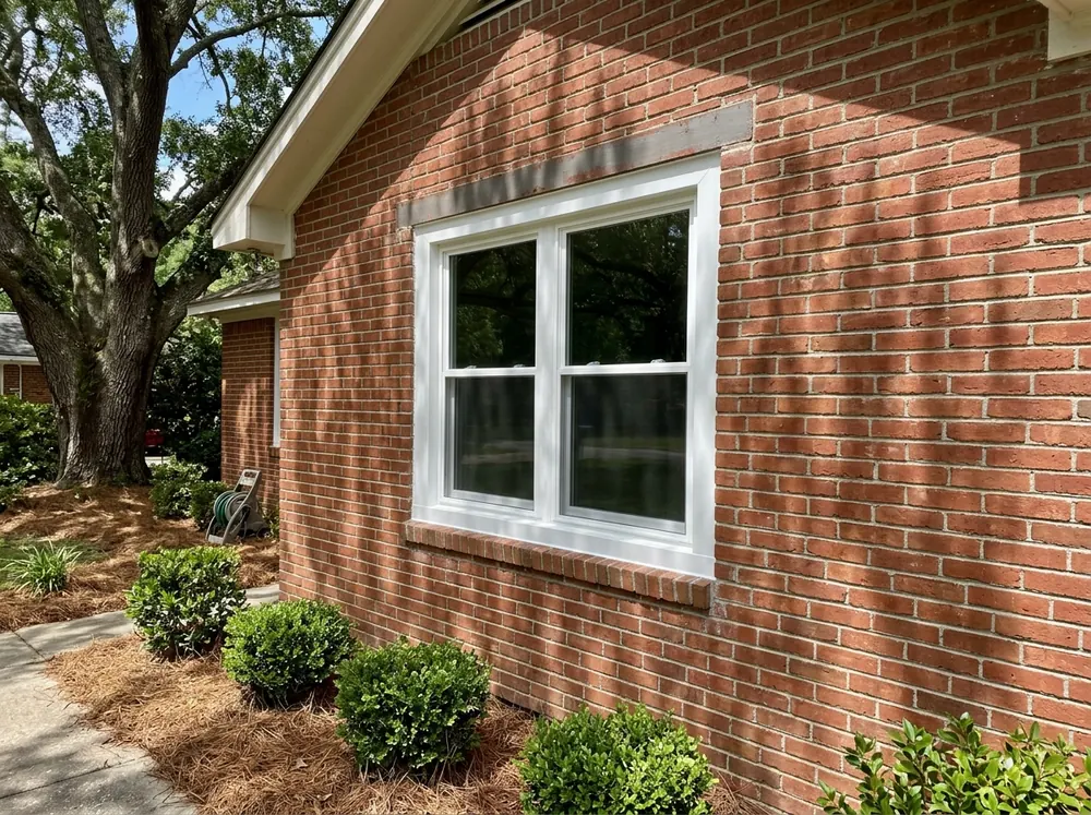 A brick ranch house window with a new white replacement window inside the old opening and white aluminum capping over the brick mold